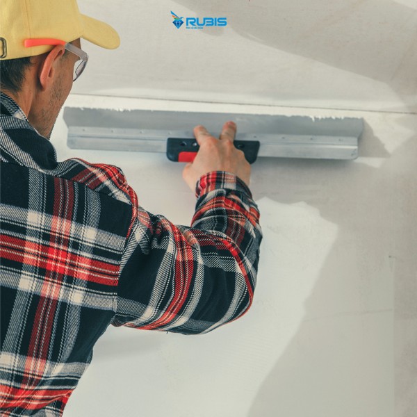 Thợ thi công bột trét tường bằng bàn gạt để tạo bề mặt phẳng trước khi sơn hoàn thiện